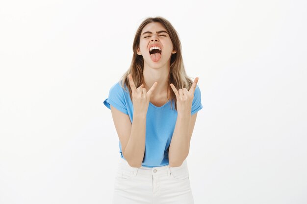 Carefree blond woman having fun, enjoying moment, showing rock-n-roll gesture