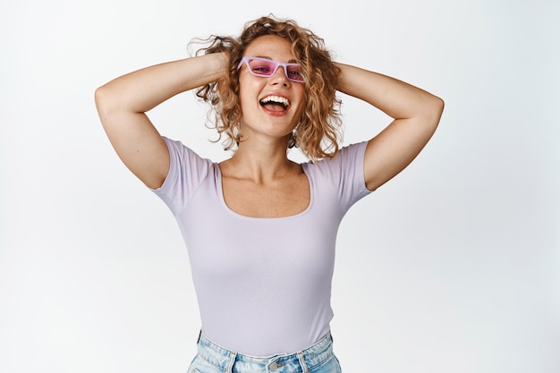 Carefree blond woman in sunglasses hold hands behind head, laughing and smiling happy, enjoying free time, relaxing, resting white.