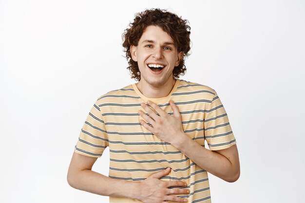 Carefree curly guy laughing and smiling enjoying watching something funny standing in tshirt over white background