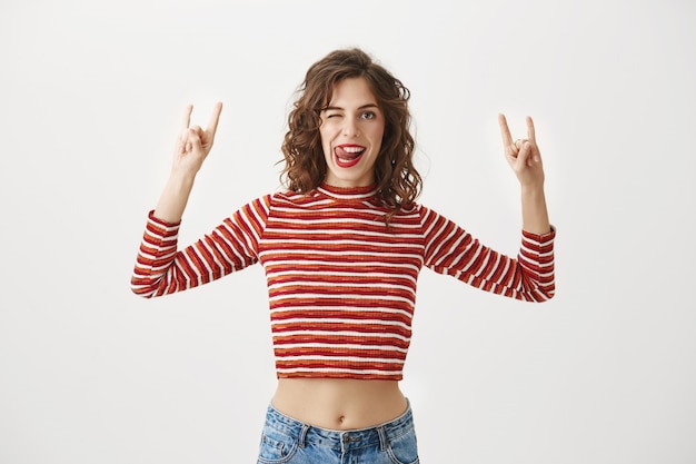 Carefree excited woman smiling and showing rock-n-roll gesture