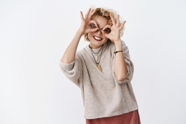 Carefree funny and beautiful joyful girl with short blond hair and dark lipstic smiling broadly showing glasses on eyes with circles fooling around and feeling playful.