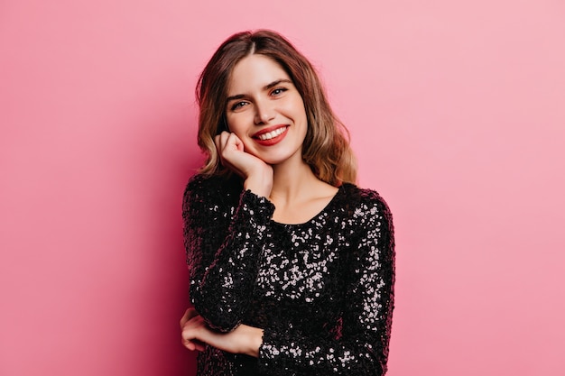 Carefree girl in black dress smiling. Elegant female model posing on pink wall.