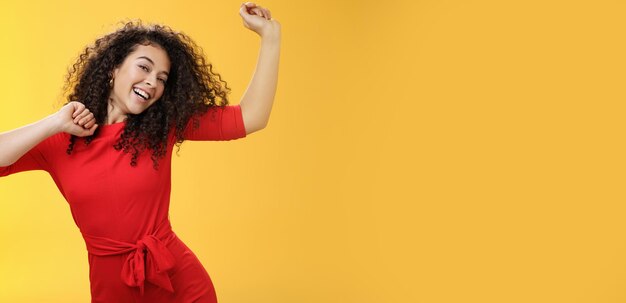 Carefree girl feeling uplifted and joyful dancing in red dress raising hands up happily tilting head