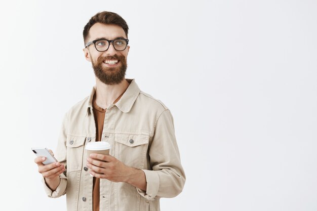 Carefree handsome bearded man in glasses posing against the white wall