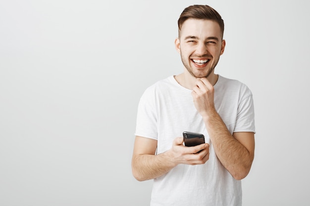 Carefree handsome guy laughing as using mobile phone application