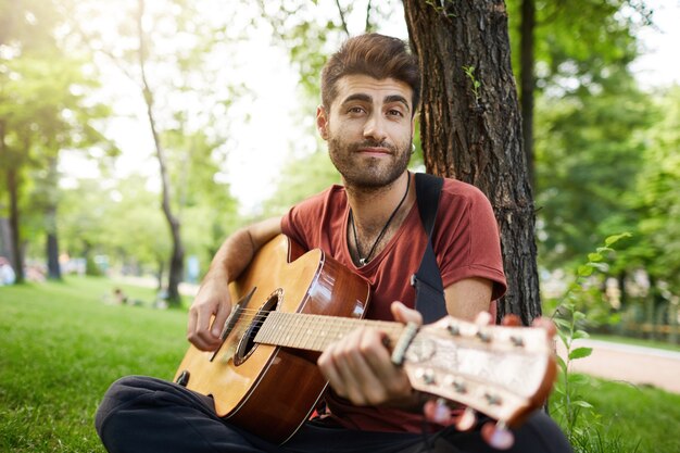 Беззаботный красивый парень играет на гитаре в парке