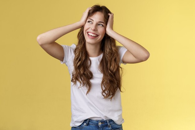 Carefree happy attractive smiling girl hold head curly hairstyle turn away upper left corner sunny summer day excellent lucky weekends standing amused excited adventures start yellow background