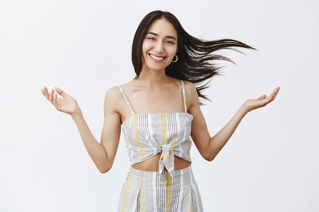 Free photo carefree happy and emotive young female with hair floating on wind, speading raised hands asides and smiling broadly, enjoying windy and warm weather