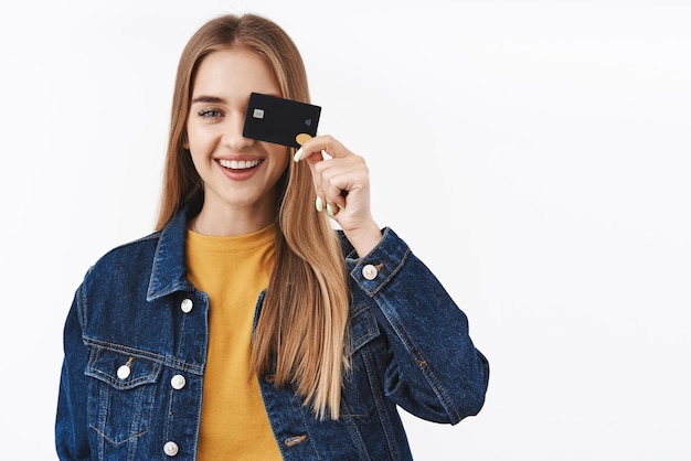 Free photo carefree and happy smiling girl showing credit card near eye finally receive payment gonna waste money place cash on deposit using cashback making investment stand white background