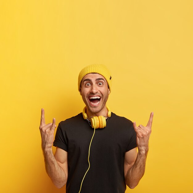 Carefree joyful guy makes rock n roll gesture, brings positive vibes, listens rock music in headphones