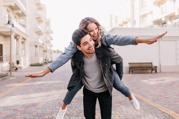 Carefree man in black jacket walking around with girl. Outdoor portrait of blissful couple enjoying weekend together.