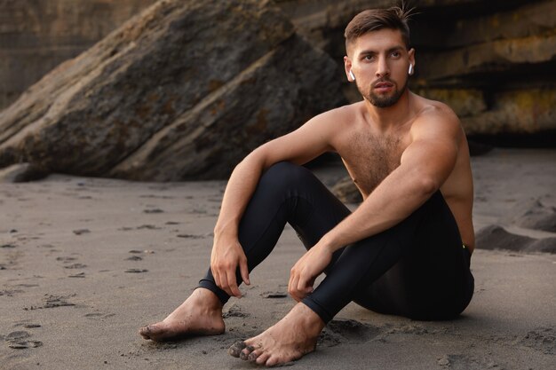 Carefree man champion sits bare foot, wears black leggings, has beard