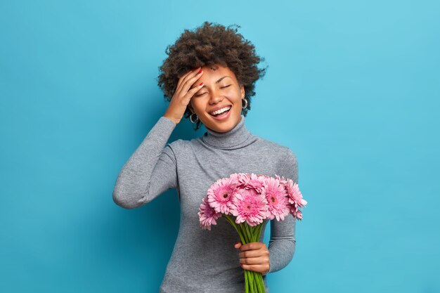 のんきな楽観的な暗い肌の民族の女性は、美しい花の花束を広く笑顔で保持します