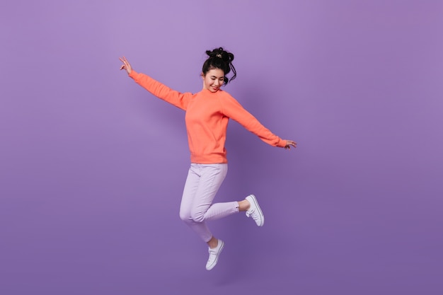 Free photo carefree pretty asian woman jumping with smile. studio shot of funny korean woman dancing on purple background.