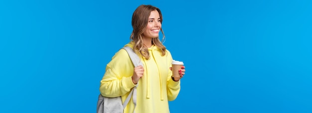 Бесплатное фото Беззаботная симпатичная молодая студентка пьет кофе из бумажного стаканчика во время учебы в университете