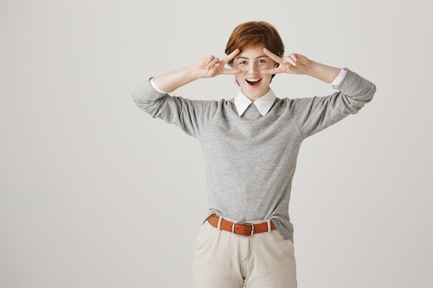 Carefree redhead girl with short haircut posing against the white wall