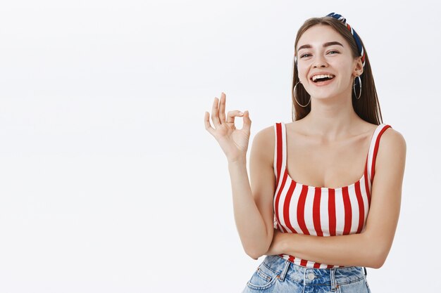 Carefree relaxed and joyful european pinup woman in headband and striped red top showing okay gesture