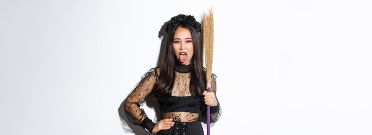 無料Photo 魔女の衣装を着てほうきを持ってハロウィーン パーティーを楽しんでいる屈託のない生意気なアジアの女性