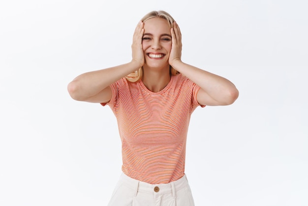 Carefree silly cute caucasian woman in striped tshirt with tattoos squeez cheeks and smiling joyfully look pleased and cheerful having fun being happy enjoy life white background