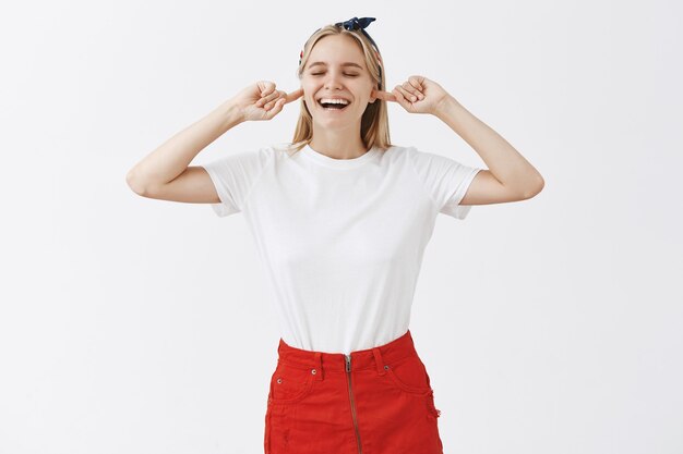 Carefree smiling young blond girl posing against the white wall