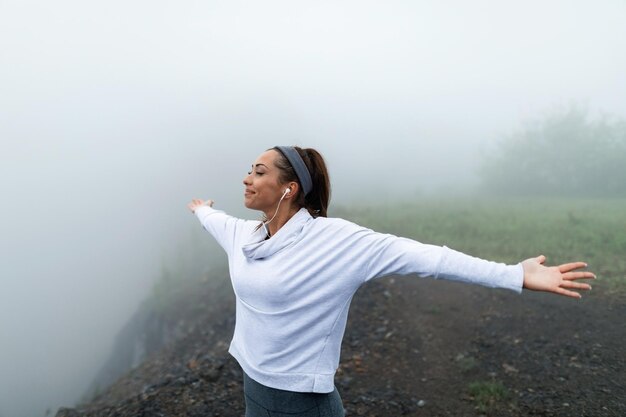 Carefree sportswoman with arms outstretched standing on a cliff in foggy weather Copy space