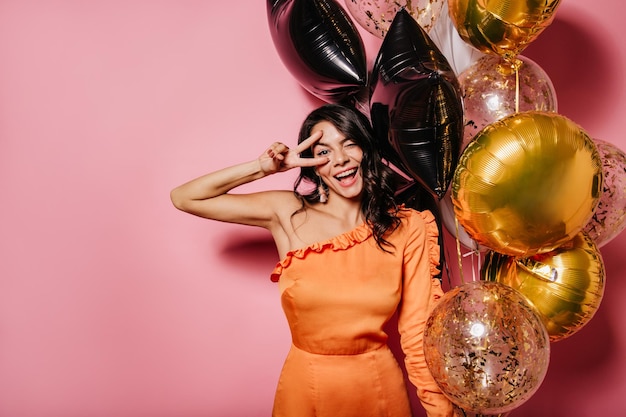 Foto gratuita ragazza abbronzata spensierata che si gode la festa con un sorriso affascinante donna latina con palloncini che ridono su sfondo rosa