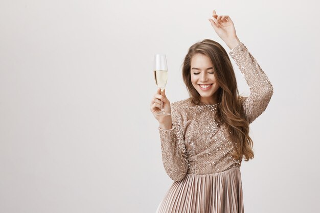 Carefree woman dancing in evening dress, holding champagne glass