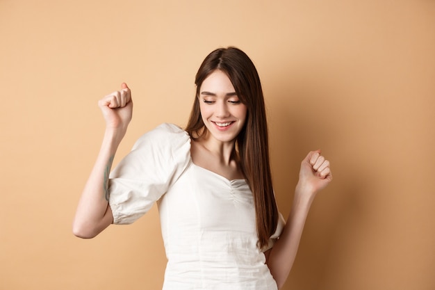 Carefree woman dancing and having fun close eyes and smiling standing on beige background