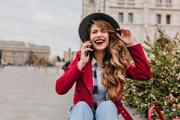 Carefree woman in elegant hair sitting on the ground and talking on phone