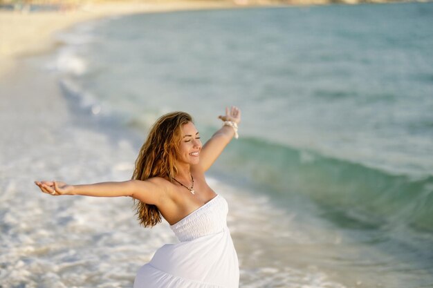 Беззаботная женщина чувствует себя свободной, стоя на берегу с распростертыми объятиями