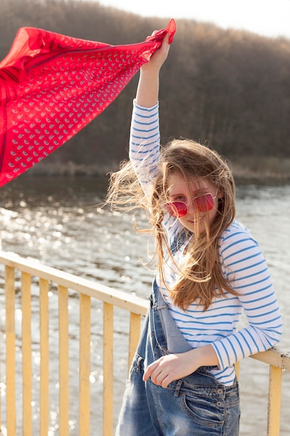 Carefree woman holding scarf in the wind by the lake