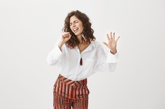 Carefree woman singing as if holding a microphone, having fun