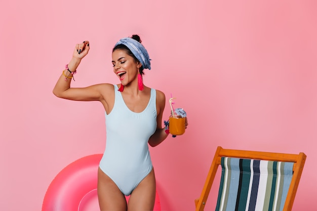 Carefree woman in swimsuit dancing on pink background