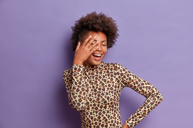 Carefree young Afro American woman covers face with palm, closes eyes and giggles positively, enjoys life