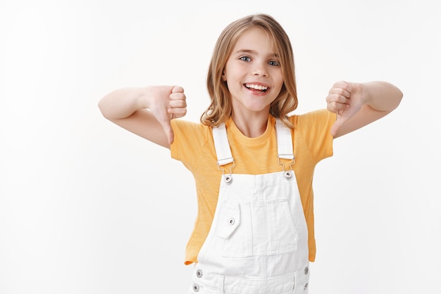 Free photo carefree young blond girl showing thumbs down, mocking team who lost, smiling broadly satisfied friend bad result loser, express dislike