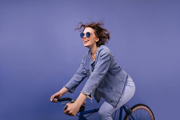 Carefree young lady in trendy glasses riding on bike Amazing funny girl sitting on bicycle and smiling