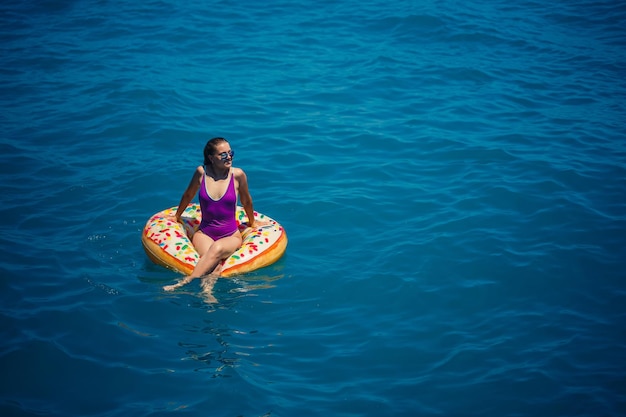 Беззаботная молодая женщина наслаждается расслабляющим днем в море, плавая на надувном кольце концепция морского отдыха Premium Фотографии