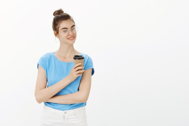 Carefree young woman in glasses drinking coffee and smiling