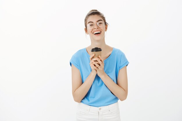 Carefree young woman in glasses drinking coffee and smiling