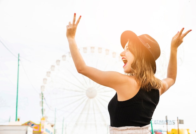 Free photo carefree young woman showing peace sign at amusement park