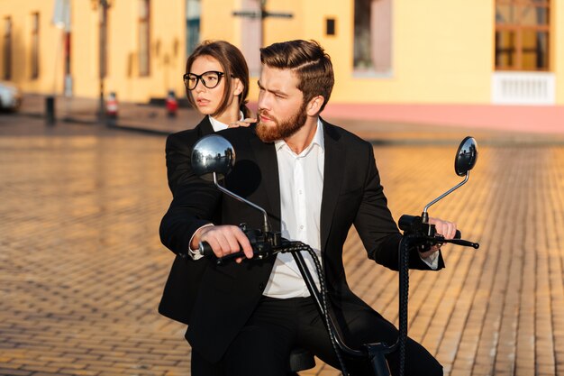 Careful business couple rides on modern motorbike in park