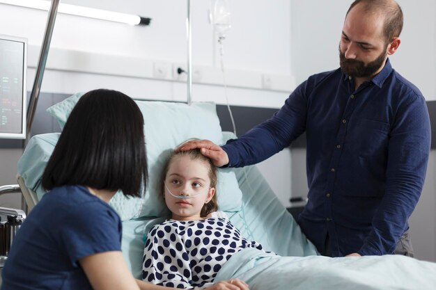 回復期間について病気の娘と話している注意深い両親。回復病棟での診察結果や病気の治療について、病気の子供患者と話し合う若い母親と父親。