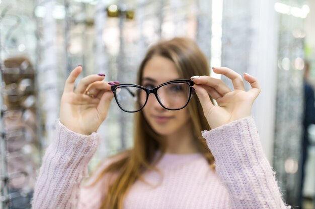 Осторожная молодая студентка готовится к учебе в колледже и примерить новые очки для своего идеального образа в профессиональном магазине.