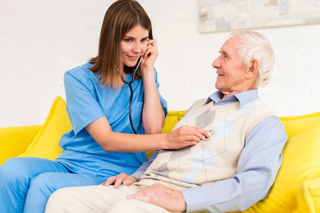 Free photo caregiver using stethoscope on old man