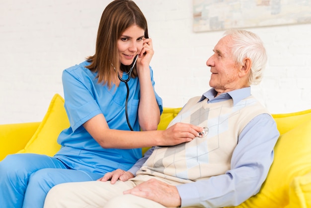 Caregiver using stethoscope on old man