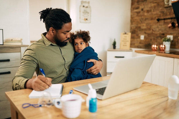 Caring black father taking care of his ill small daughter while working at home