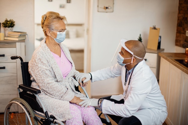 코로나바이러스 전염병 동안 요양원에서 휠체어를 탄 노인 여성과 이야기하는 돌보는 의사