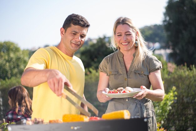 Caring husband and wife making BBQ in backyard