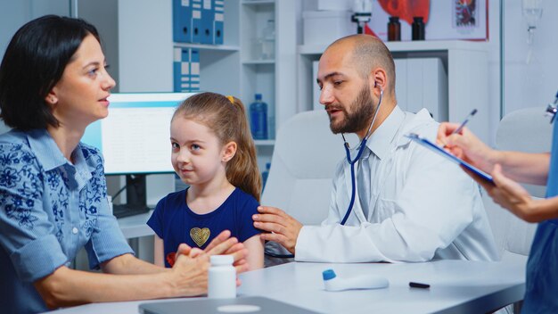 Заботливый врач консультирует девушку в офисе со стетоскопом, проверяя дыхание. Медицинский специалист, оказывающий медицинские услуги, консультация, диагностическое обследование, лечение в больничном кабинете.