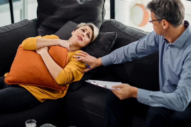 Caring psychiatrist consoling sad woman during therapy session at his office